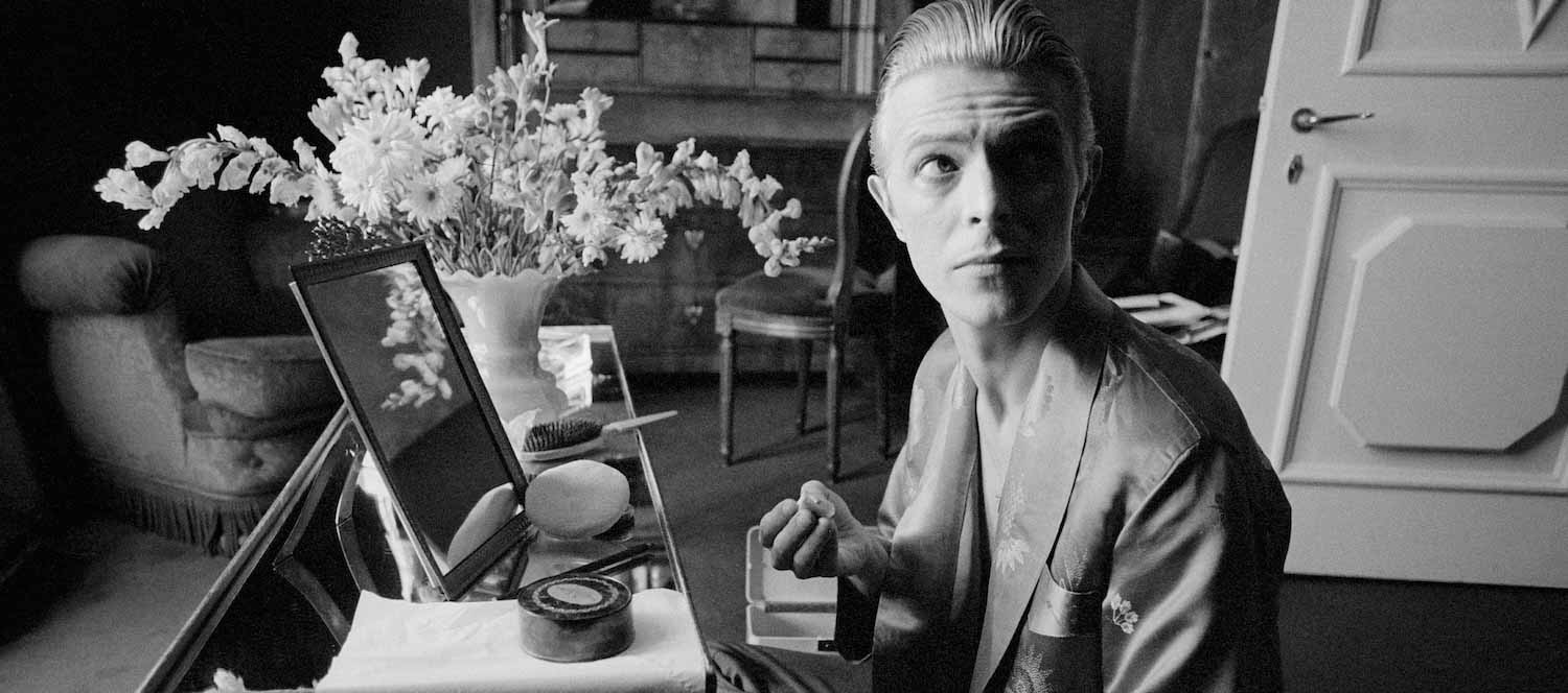 Bowie mentre si prepara il trucco nella sua suite d’albergo prima di un improvvisato servizio fotografico a Parigi (1976)