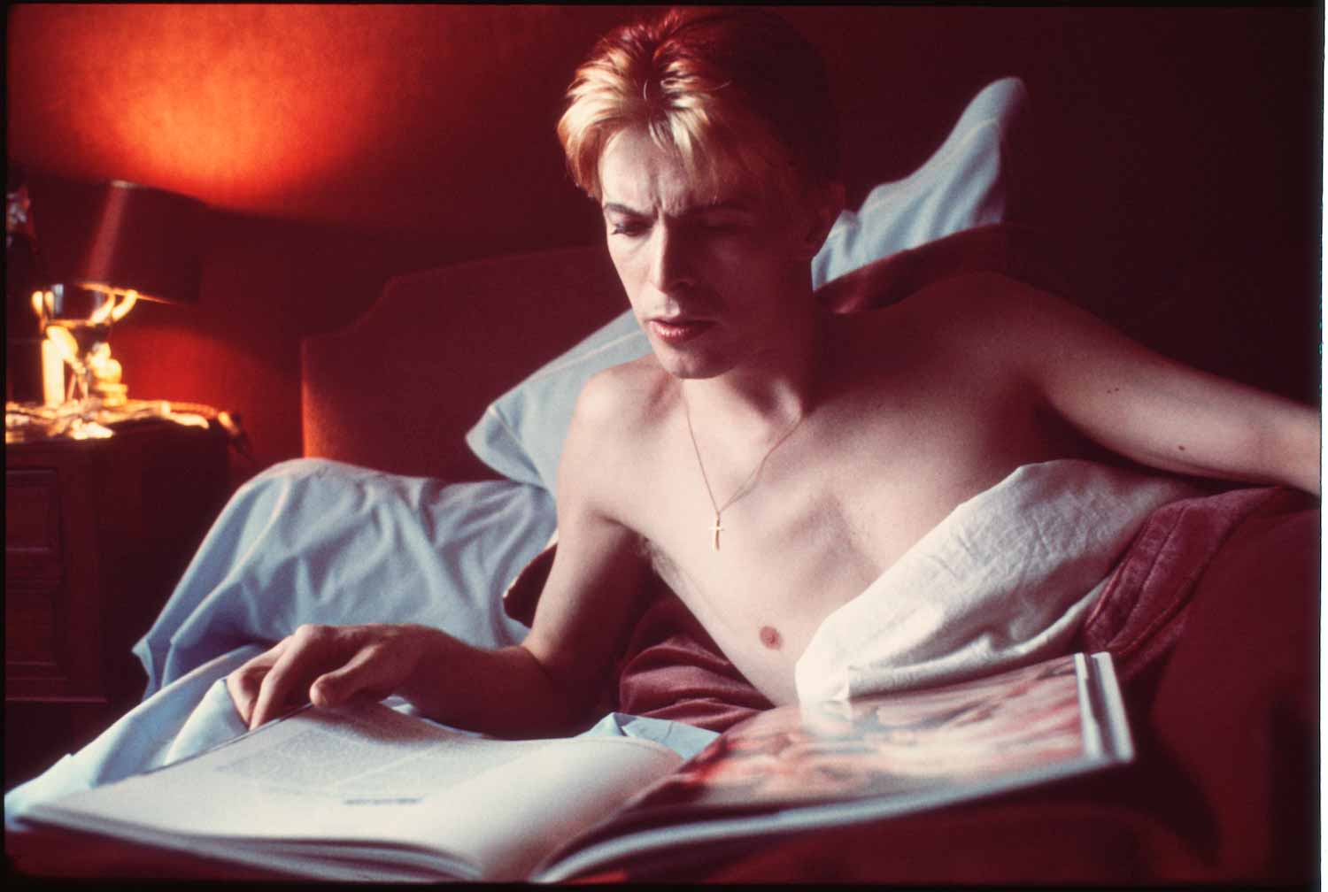 David Bowie legge un libro nel suo letto durante una rara mattinata tranquilla nella sua suite in un hotel di Parigi (1976)