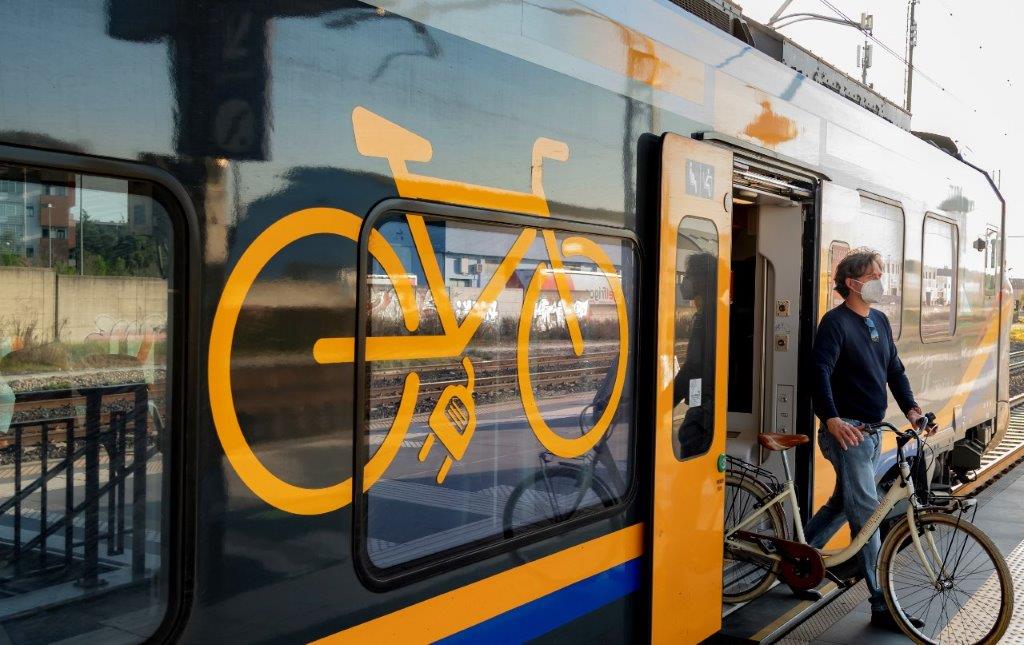 Ciclista con bici in uscita da un treno regionale