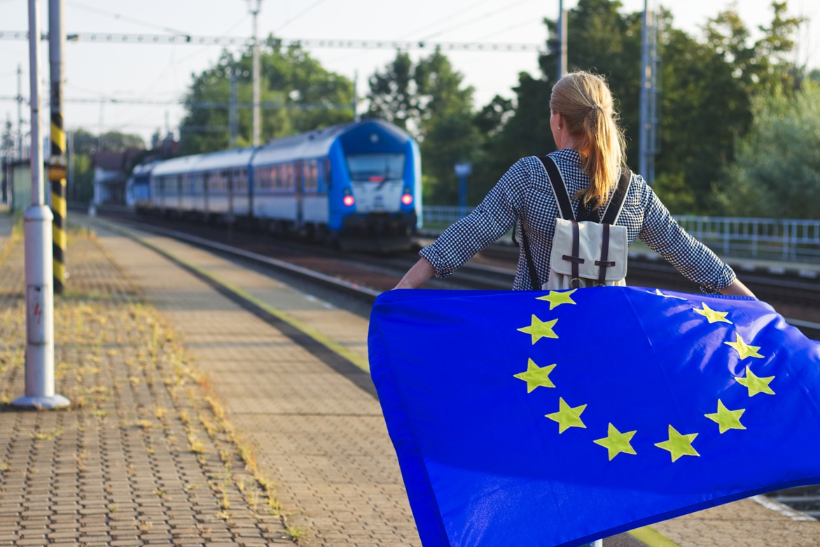 Ragazza con bandiera dell'Europa alle spalle e un treno di fronte