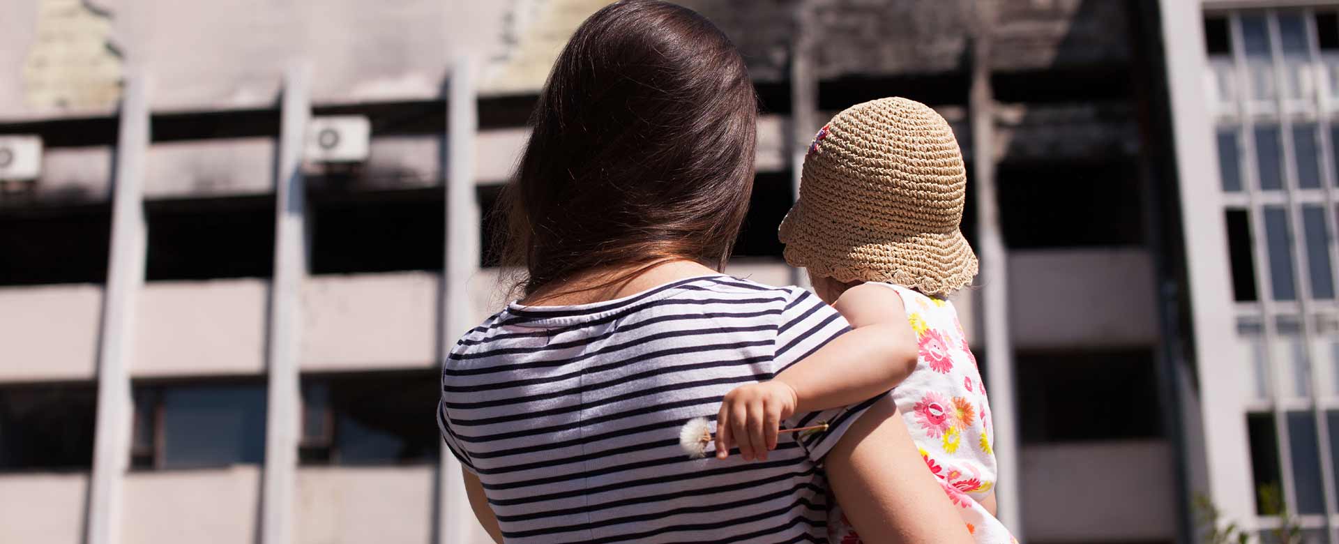 Una madre e la sua bambina guardano una costruzione distrutta di Mariupol