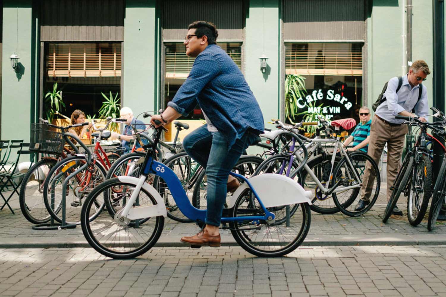 Uomo in bici, davanti a un bar al di fuori del quale sono parcheggiate diverse biciclette